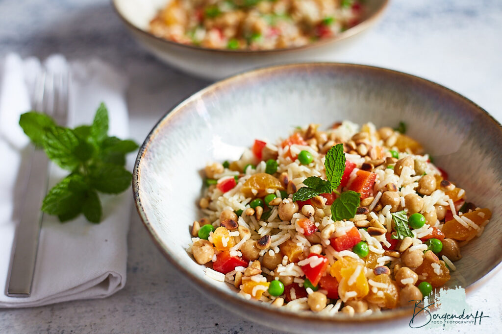 Salat bestående af ris med kikærter ristet med krydderi, abrikoser i mindre stykker, ærter, pinjekerner, peberfrugt i tern og mynte.